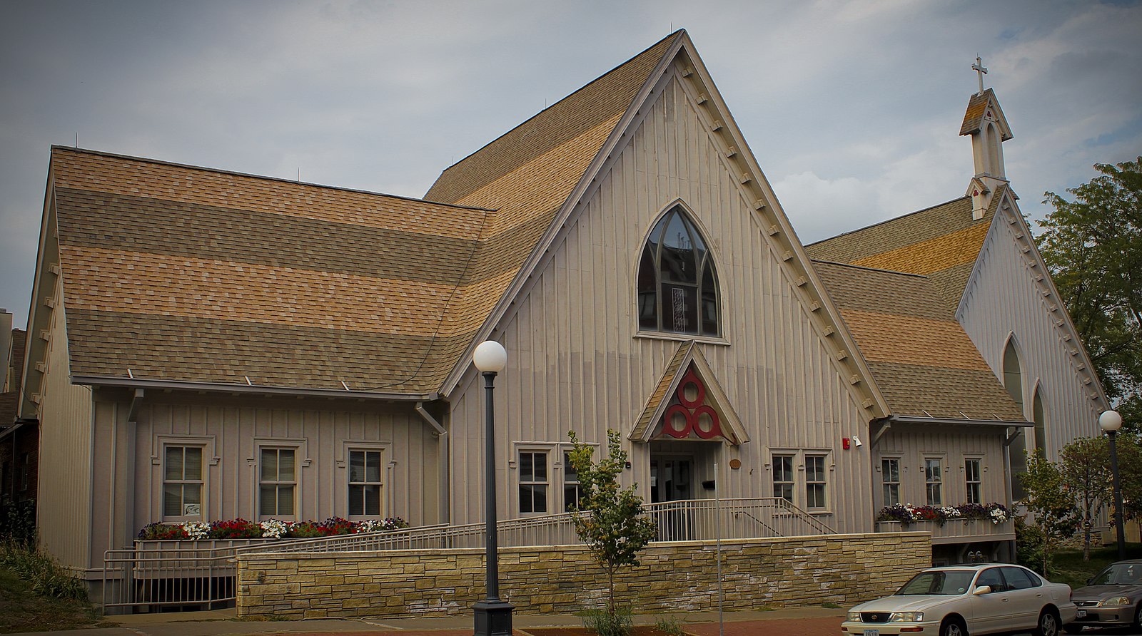 A wooden gothic-style church on a car-lined street.