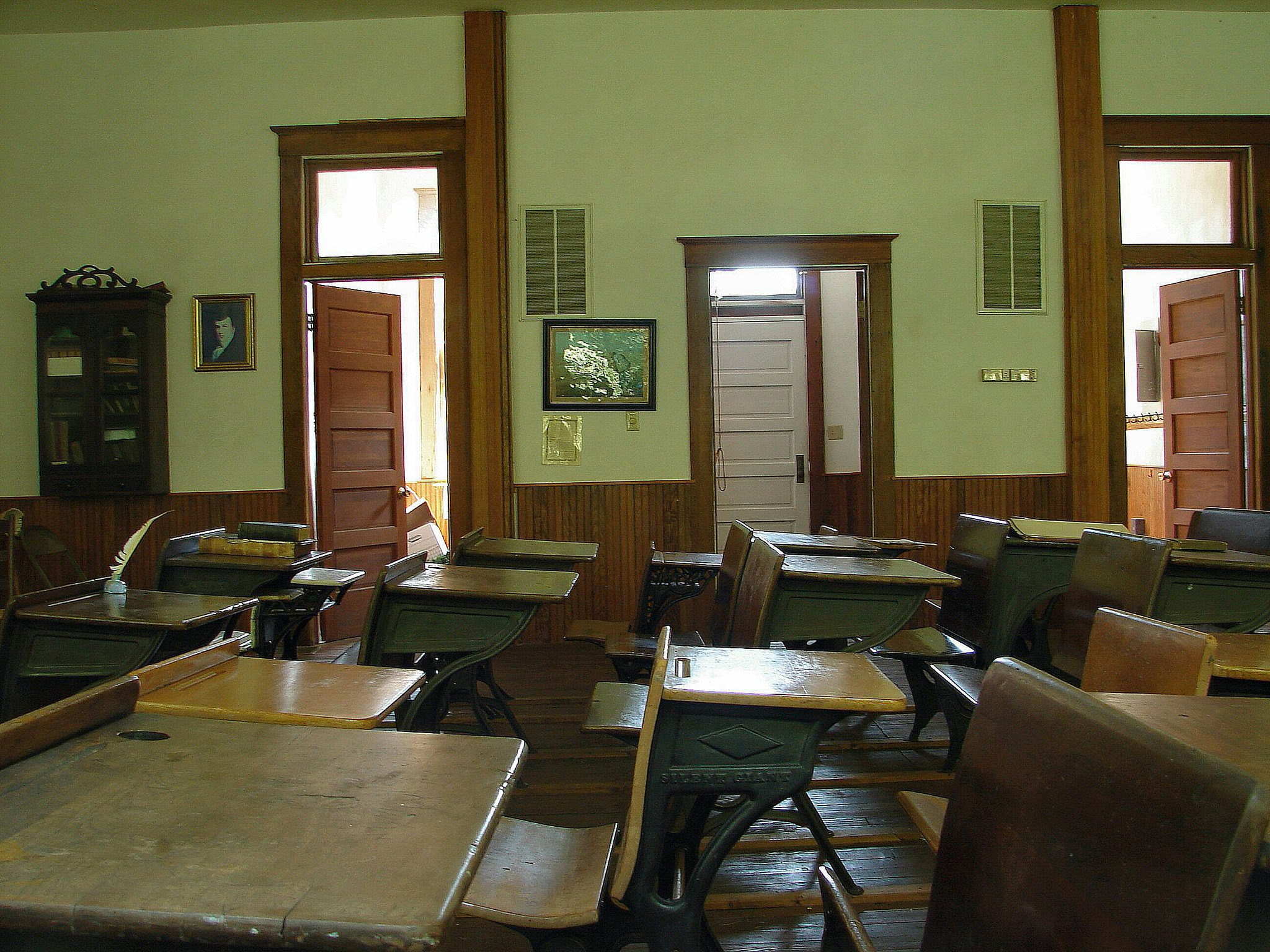 an empty old-fashioned one-room schoolhouse with light shining throuhg a window on one desk